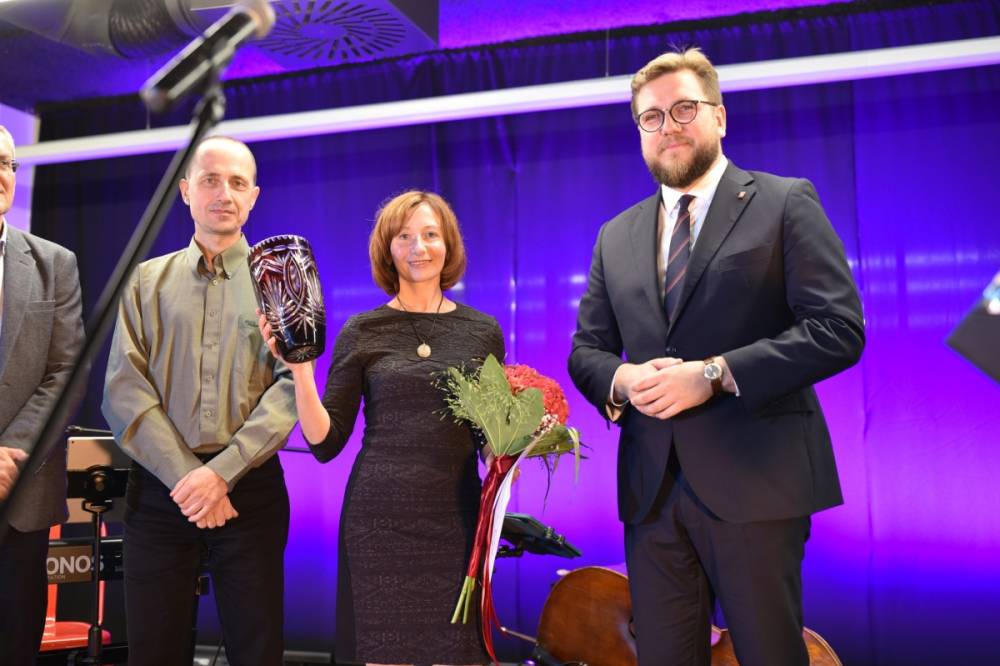 Laureatka konkursu stoi na scenie z prezydentem Piotrkowa Tryb. oraz osobami z jury. Wszyscy pozują do zdjęcia. Główna zwyciężczyni trzyma w rekach bukiet oraz rubinowy wazon.