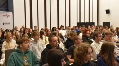 Widok publiczności. Młodzież siedzi w rzędach, zwrócona przodem do sceny. Uczestnicy są ubrani swobodnie - niektórzy noszą bluzy z kapturem, inni t-shirty.