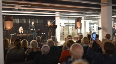 Trzy kobiety występują na scenie. Kobieta stojąca w środku śpiewa do mikrofonu, a kobiety po jej bokach grają na instrumentach. Kobieta po lewej na keyboardzie, a kobieta po prawej na skrzypcach. Widać również część publiczności. Ktoś z widowni robi zdjęcie telefonem.