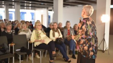 Osoba prowadząca spotkanie stoi przodem do publiczności i przemawia do mikrofonu.