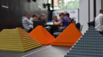 Na pierwszym planie widzimy cztery piramidy, każda w innym kolorze. W tle widać uczestników siedzących przy stoliku.