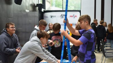 Uczestnicy budują wysoką wieżę z niebieskich klocków.