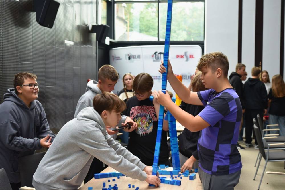 Uczestnicy budują wysoką wieżę z niebieskich klocków.