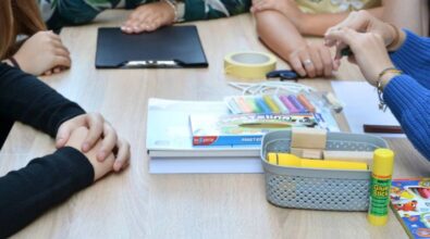 Zbliżenie na stolik uczestników, na którym leżą m.in. duży notatnik, blok, plastelina, nożyczki, taśma oraz plastikowy koszyczek z latarka i drewnianymi klockami. Dookoła widać ręce uczestników.