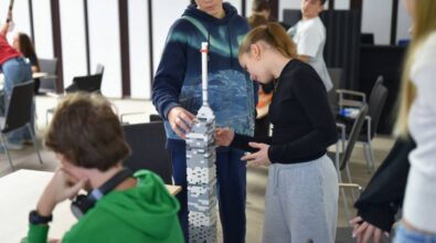 Uczestnicy budują wysoką wieżę z szarych klocków, która stoi na podłodze.