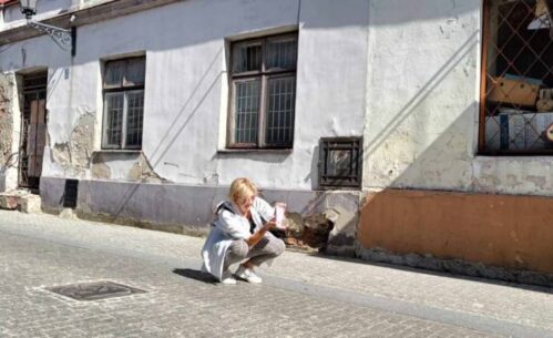 Zdjęcie na jednej z uliczek Rynku Trybunalskiego. Osoba robiąca zdjęcie kuca na brukowanej ulicy, w tle widać obdrapany budynek.