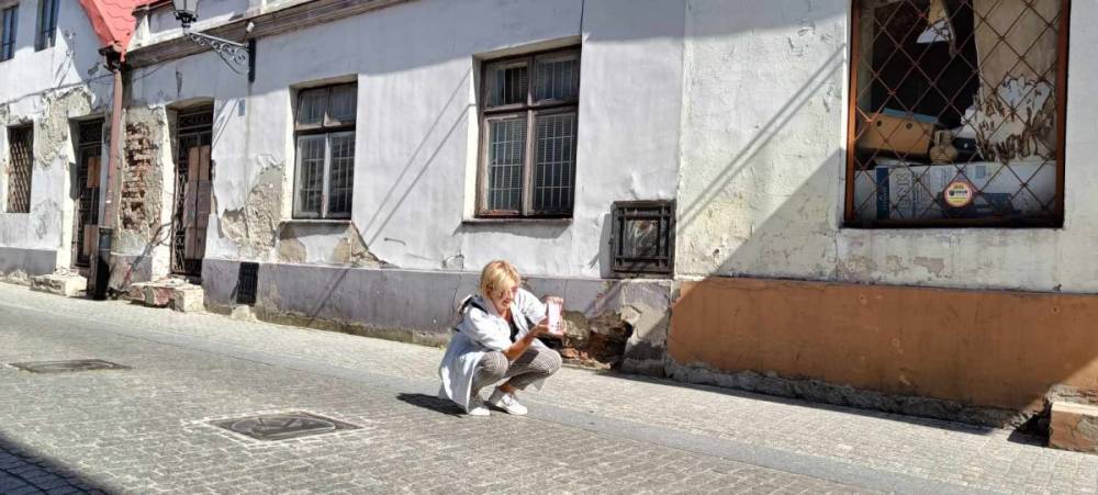 Zdjęcie na jednej z uliczek Rynku Trybunalskiego. Osoba robiąca zdjęcie kuca na brukowanej ulicy, w tle widać obdrapany budynek.
