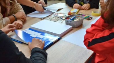 Zbliżenie na stolik uczestników, na którym leżą m.in. duży notatnik, blok, plastelina, nożyczki, taśma oraz plastikowy koszyczek z latarka i drewnianymi klockami. Dookoła widać ręce uczestników.