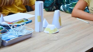 Na stoliku przed uczestnikami stoją posklejane z papieru przestrzenne figury geometryczne.