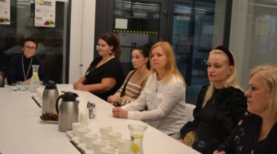 Grupa osób siedzi przy stoliku, na którym stoją filiżanki, karafki z wodą, metalowe dzbanki oraz słodkości.