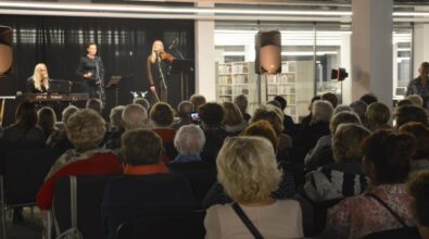 Trzy kobiety występują na scenie. Kobieta stojąca w środku śpiewa do mikrofonu, a kobiety po jej bokach grają na instrumentach. Kobieta po lewej na keyboardzie, a kobieta po prawej na skrzypcach. Widać również część publiczności.