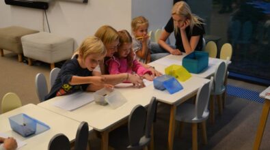 Dzieci wraz z dorosłymi siedzą przy stoliku i wykonują pracę plastyczną.