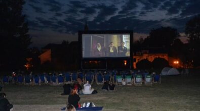 Ludzie siedzący na leżakach oglądają film na dużym telebimie. Jest wieczór, w oddali widać oświetlone budynki. Parę osób siedzi na trawie.