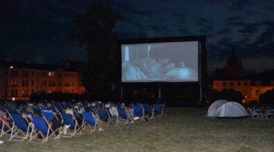Ludzie siedzący na leżakach oglądają film na dużym telebimie. Jest wieczór, w oddali widać oświetlone budynki.