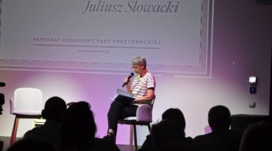 Kobieta siedzi na scenie i czyta fragment 