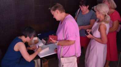 Kilka osób stoi przy stoliku, przy którym autorka podpisuję książkę.