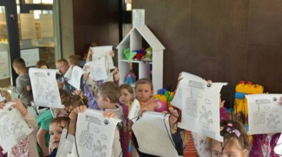 Dzieci pozują do zdjęcia. Wszystkie trzymają białe worki ze sznurkiem, na których znajdują się nadruki z zamkiem i smokiem.