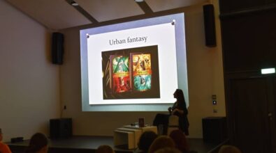 Widok na kolejny slajd prezentacji, osobę prowadzącą oraz publiczność.