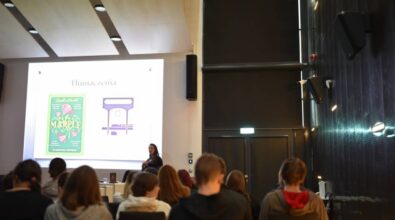 Widok na kolejny slajd prezentacji, osobę prowadzącą oraz publiczność.