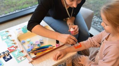 Animator wykonuje tatuaż na ręku dziecka. Na stoliku widać pędzle i kolorowe brokaty oraz różne szablony tatuaży.