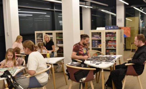 Widok na osoby siedzące przy stolikach i grające w gry planszowe.