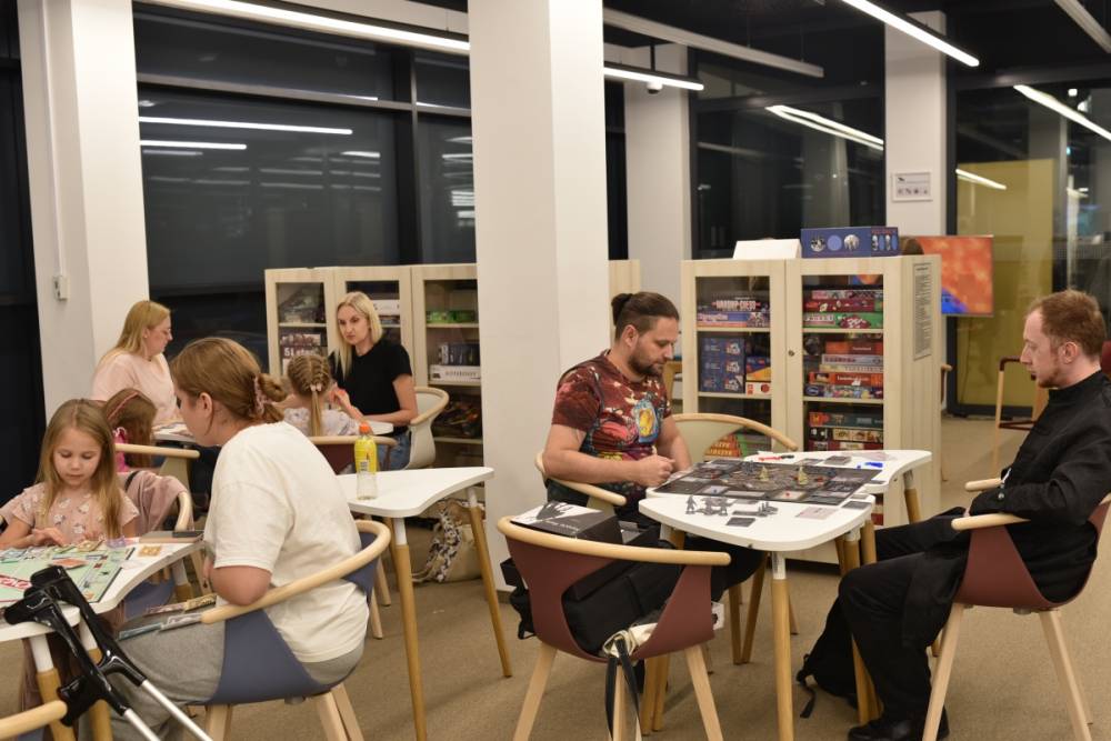Widok na osoby siedzące przy stolikach i grające w gry planszowe.
