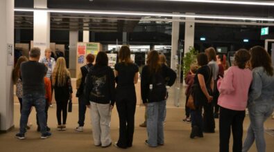 Grupę ludzi skierowana jest w stronę osoby, która do nich przemawia. W grupie są osoby w różnym wieku, ubrane swobodnie. Niektórzy trzymają torby lub butelki z wodą.