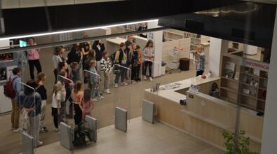 Widok z góry na grupę osób słuchających kobiety w koszuli w kratkę. Kobieta pokazuje kartkę z informacjami