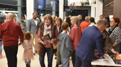 Zgromadzone osoby oglądają wystawę. Niektórzy stoją w grupkach i rozmawiają ze sobą. Parę osób trzyma broszury, inni podchodzą do stolika z broszurami.