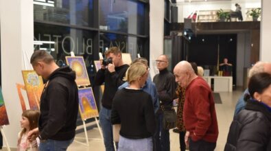Uczestnicy wystawy oglądają obrazy, młody mężczyzna robi zdjęcia, jeden z malarzy rozmawia z innymi osobami.