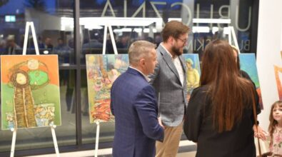 Uśmiechnięty prezydent miasta stoi z innymi osobami na tle wystawy i rozmawia.