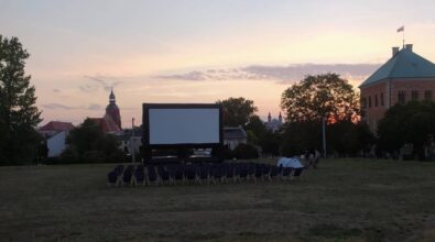 Przygotowania do kina pod chmurką. Na zdjęciu widać zamontowany telebim oraz leżaki ustawione w rzędach. W oddali widać budynki.