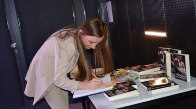 Autorka wpisuję się do kroniki pamiątkowej biblioteki. Pochyla się nad stolikiem, na którym widać kilka egzemplarzy jej książki.