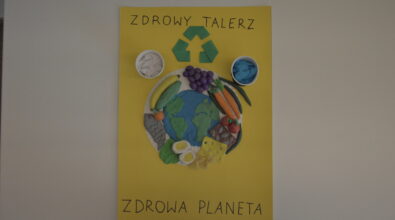 Praca konkursowa w formie przestrzennego plakatu przedstawiająca umieszczony centralnie talerz z różnymi produktami, owoce, warzywa, jajka, ser, ryba, chleb, prawdziwy makaron. Produkty otaczają planetę Ziemia. Elementy wykonane z plasteliny. Po lewo nad talerzem papierowy biały kubek z mlekiem z białej bibuły, po prawo nad talerzem papierowy czarny kubek z wodą z niebieskiej bibuły. Pośrodku zielony znak recyklingu. Czarny napis „ZDROWY TALERZ” na samej górze i „ZDROWA PLANETA” Na dole. Tło żółte.
