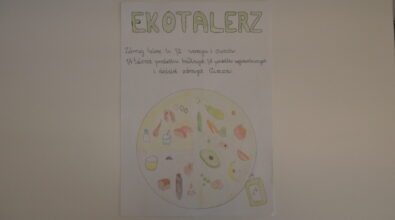 Praca konkursowa w formie plakatu przedstawiająca podzielony na 3 części talerz z różnymi produktami, warzywa, owoce, produkty zbożowe, mięso, jajko, mleko. W prawym dolnym rogu butelka oliwy z oliwek. Na górze zielony napis „EKOTALERZ” oraz dwa zdania poniżej dotyczące zasad zdrowego żywienia. Praca wykonana kredkami. Tło białe.