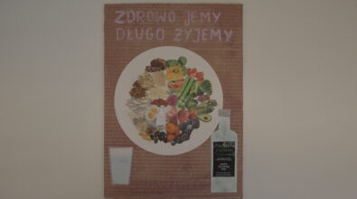 Praca konkursowa w formie plakatu przedstawiająca umieszczony centralnie biały talerz z różnymi produktami, warzywa, owoce, ryby, mleko, jajka, chleb, prawdziwa kasza, płatki owsiane, ryż, orzechy, fasola, pestki. W lewym dolnym rogu szklanka. W prawym dolnym rogu butelka oliwy z oliwek. Na górze różowy napis „ZDROWO JEMY DŁUGO ŻYJEMY”. Tło brązowa tektura.