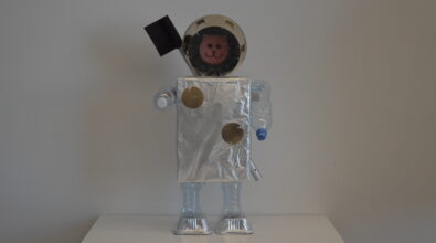 Praca plastyczna przedstawiająca kota astronautę wykonanego z materiałów recyklingowych. Tułów wykonany z kartonika obklejonego folia aluminiową. Głową jest różową gąbka w kształcie głowy kota zamknięta w plastikowym przezroczystym okrągłym pojemniku. Ręce i nogi z plastikowym butelek. Buty z aluminiowych prostokątnych foremek. Na plecach przyczepiona długa rurka z czarną chorągiewką na górze.