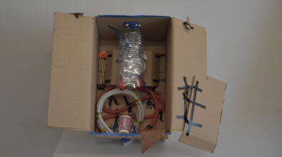 Otwarte od góry kartonowe pudełko, w którym znajduje się konstrukcja wykonana z plastikowej butelki, słomek i dwóch czerwonych balonów. Pod nimi umieszczony jest zegar. Niżej widoczna jest dalsza część konstrukcji z białego i czerwonego węża harmonijkowego oraz papierowego kubeczka, połączonych taśmą. Całość przypomina wnętrze ludzkiego ciała.”